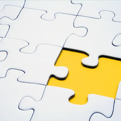 A jigsaw of white pieces with a single golden piece dropped into place.